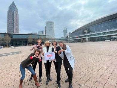 Gruppenbild von Mitarbeitenden der Messe Frankfurt und des Frankfurt Convention Bureaus mit dem Messegelände im Hintergrund und einem Bild in der Hand, das SIBOS in Frankfurt willkommen heißt