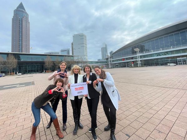 Group photo of employees of Messe Frankfurt and the Frankfurt Convention Bureau with the exhibition grounds in the background and a picture in their hands welcoming SIBOS to Frankfurt