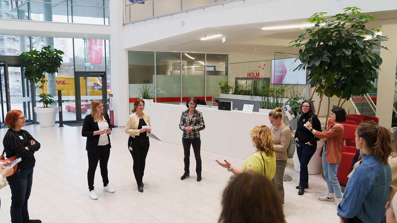 Eine Gruppe von Menschen steht in einem Foyer und tauscht sich in einer interaktiven Diskussion aus.