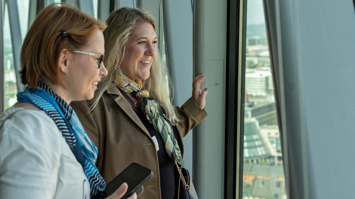 Zwei Personen blicken aus Hochhausfenster auf die Stadt.