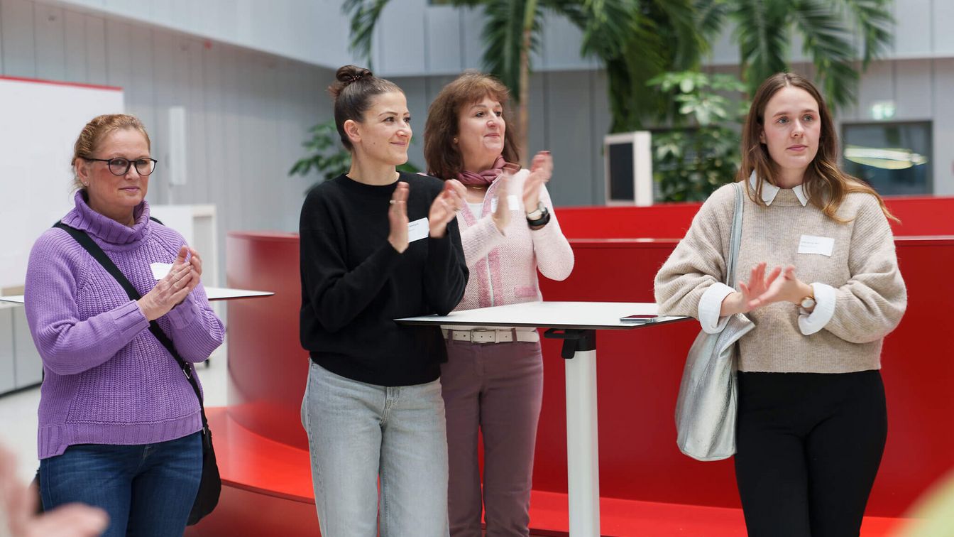 Vier Frauen stehen an einem Stehtisch und applaudieren.